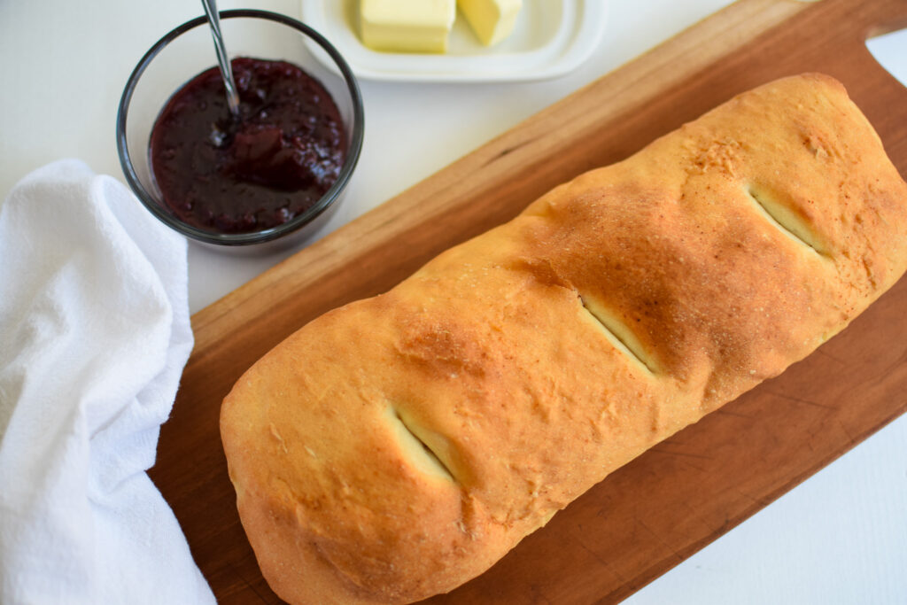 loaf of bread on a cutting board with a bowl of jelly