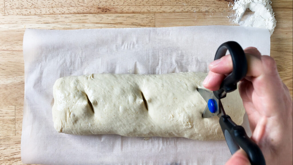 bread dough being cut on top to go in over