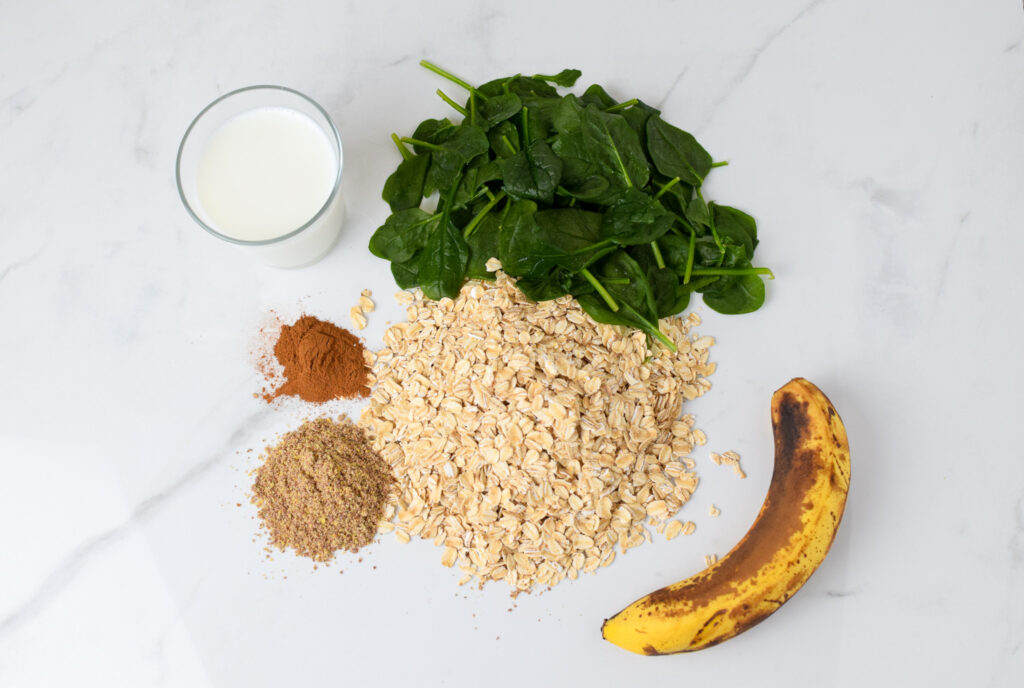 oats, spinach, banana milk, cinnamon and flax in piles on a counter to make banana pancakes for a baby