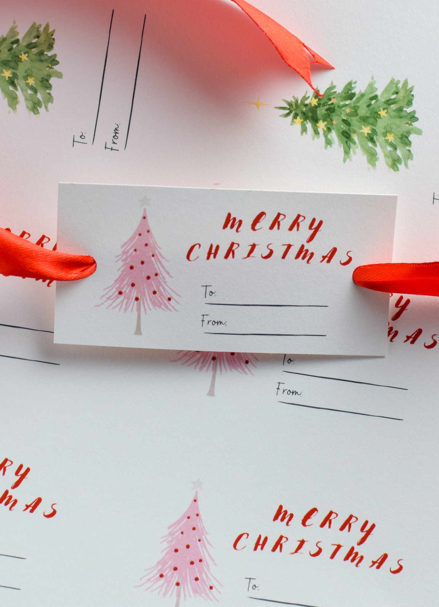 Christmas gift tag with ribbon through it on top of a sheet of uncut Christmas gift tags